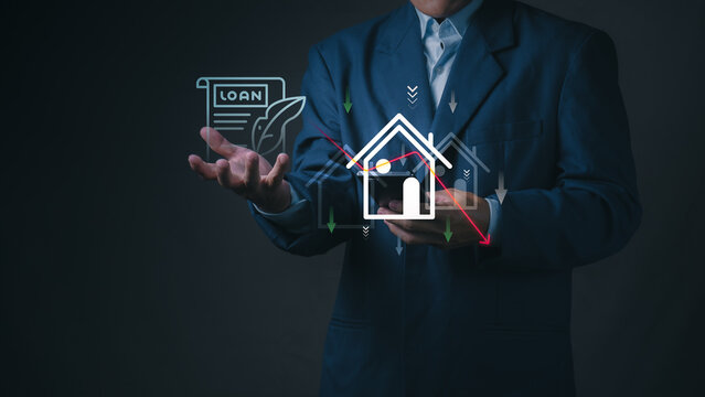 Businessman holds smartphone with virtual house, mortgage loan document, and down trend arrow for property investment, real estate crisis, and interest rate drop.