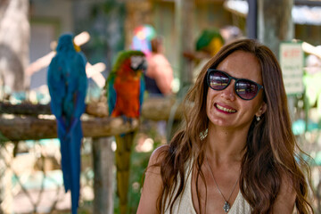 Smiling woman wearing sunglasses near colorful macaws © Moiseii Production