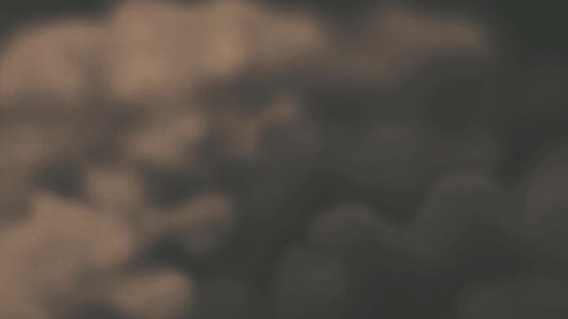 A soft abstract background featuring slow moving dark grey and brownish smoke clouds in a fluid motion loop