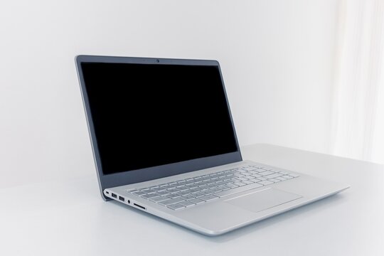 Open silver laptop with black screen on plain desk