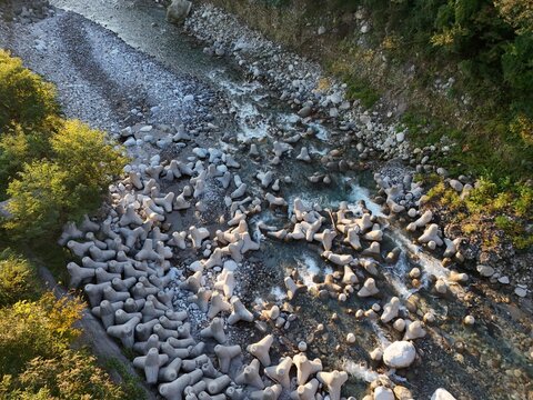 Viewed directly from above, rows of pale interlocking concrete units sit among river stones and shallow flowing water.