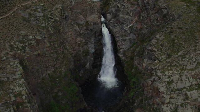 Powerful Kurkure waterfall cascades down rugged rocky cliffs into a dark canyon pool within the scenic wilderness of the Altai Republic in Russia during cloudy daylight