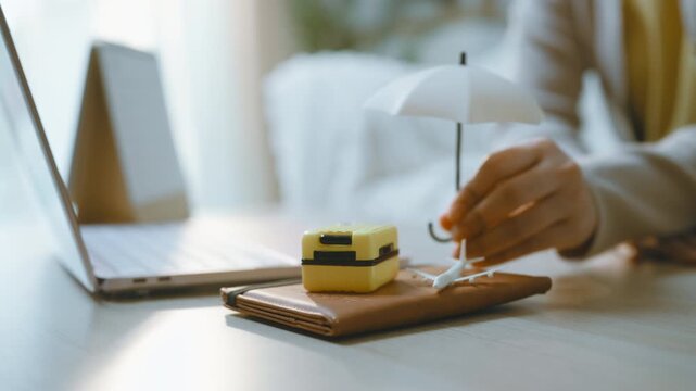 Travel planning is symbolized by a miniature suitcase and airplane beside a laptop, with hands arranging the trip accessories on a notebook as travel preparation takes shape on a domestic table.