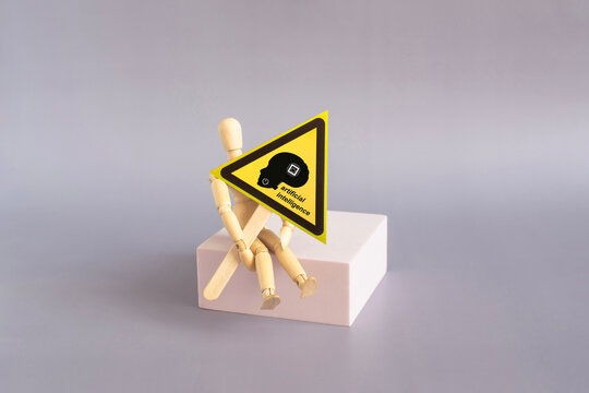 In the doll's hands is a "dangerous AI" warning sign: a yellow triangle on a stand.