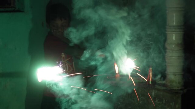 Young boy holding a sparkling firecracker with green smoke during diwali