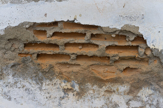 Damaged white wall and red bricks peeling and exposing on an outdoor building structure depicting structural decay