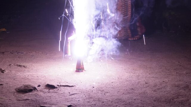 Young boy lighting an anar fountain firework during diwali