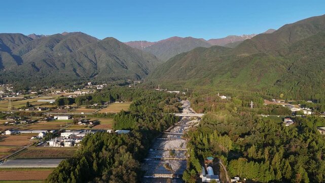 A river flows between dense riverside trees with scattered rural buildings and agricultural plots on either side.