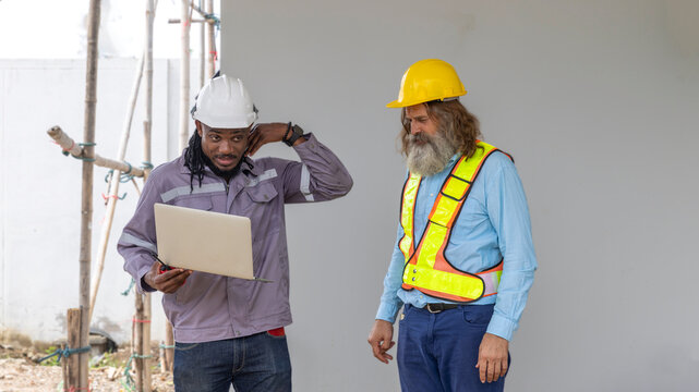 Two construction workers from different generations using a laptop to review progress together, highlighting teamwork, shared experience, and learning in a contruction place