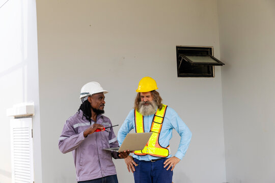 Two construction workers from different generations using a laptop to review progress together, highlighting teamwork, shared experience, and learning in a contruction place