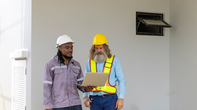 Two construction workers from different generations using a laptop to review progress together, highlighting teamwork, shared experience, and learning in a contruction place