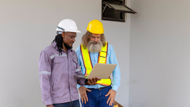 Two construction workers from different generations using a laptop to review progress together, highlighting teamwork, shared experience, and learning in a contruction place