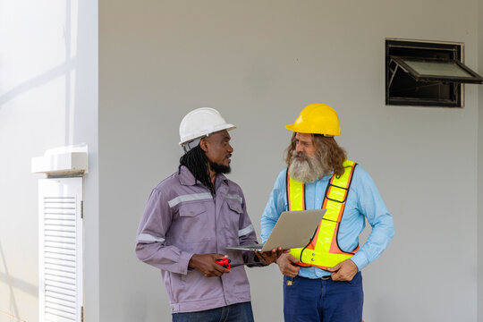Two construction workers from different generations using a laptop to review progress together, highlighting teamwork, shared experience, and learning in a contruction place