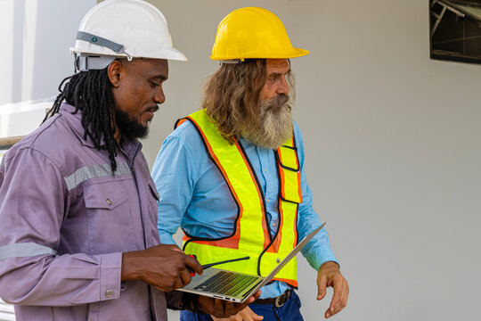 Two construction workers from different generations using a laptop to review progress together, highlighting teamwork, shared experience, and learning in a contruction place