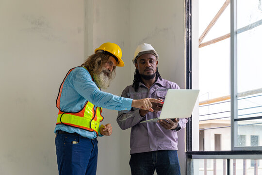 Two construction workers from different generations using a laptop to review progress together, highlighting teamwork, shared experience, and learning in a contruction place