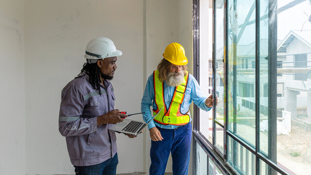 Two construction workers from different generations using a laptop to review progress together, highlighting teamwork, shared experience, and learning in a contruction place