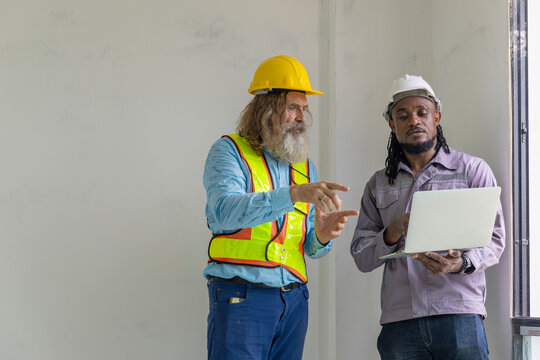 Two construction workers from different generations using a laptop to review progress together, highlighting teamwork, shared experience, and learning in a contruction place