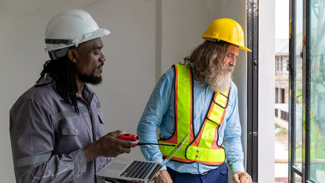 Two construction workers from different generations using a laptop to review progress together, highlighting teamwork, shared experience, and learning in a contruction place
