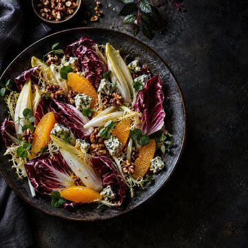 Winter salad with radicchio, endive, orange segments, walnuts, blue cheese on dark rustic plate, moody food flat lay