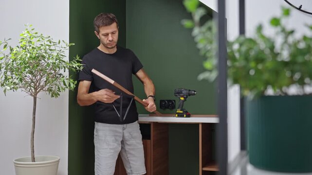Man looking at a wooden shelf and metal bracket before mounting it on the wall