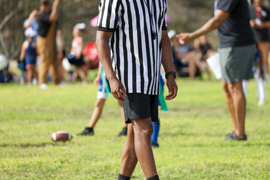 Referee in Black and White Striped Shirt Walking on Youth Flag Football Field.