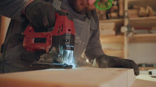 Man operates jigsaw to cut wood. close up view shows tool in action on wooden boards with workshop tools and materials visible in background joiner woodworking
