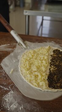 Chef transferring traditional half-cheese and half-zaatar manakish onto a pizza peel before baking it in a hot oven at a Middle Eastern restaurant.