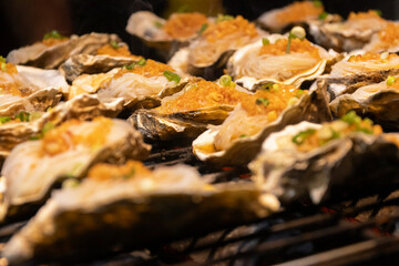 Grilled oyster with garlic topping and scallion garnish on shell, savory seafood dish served hot, appetizing smoky aroma and golden crust © pjjaruwan