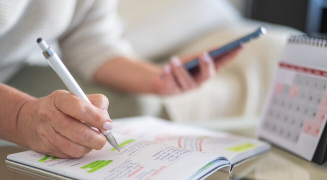 Woman organizing weekly tasks and appointments in a planner while holding a smartphone, representing efficient time management and productivity in a modern work environment