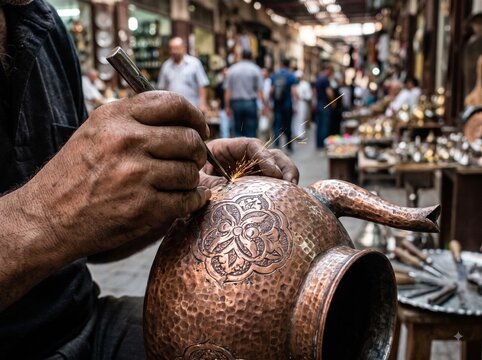 Close-up of artisan hands engraving intricate traditional patterns on copper teapot in Moroccan souk