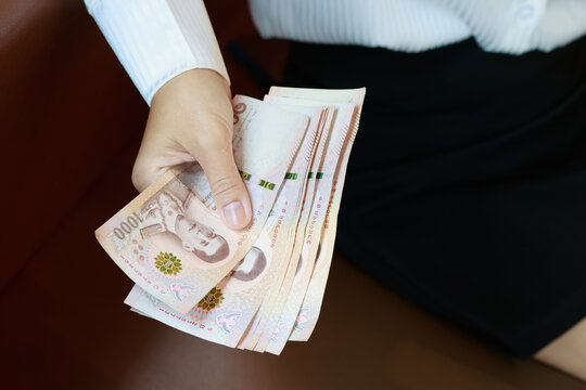 Working woman or Office lady holding Thai baht banknotes, representing finance, income, salary, savings, investment, money, cash, spending, personal budgeting, and everyday economic concepts, close-up