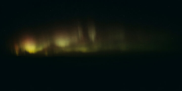 Faint aurora borealis displaying soft green and yellow light streaks against a deep night sky