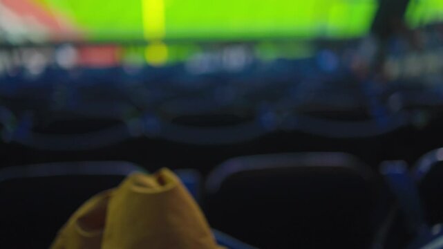 View from the upper deck of a professional baseball stadium with empty blue seats, focusing on a bright green field and a spectator wearing a yellow hat watching the game