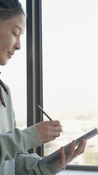 Vertical video: Tapping stylus, artist in green top drawing on tablet by window, headset
