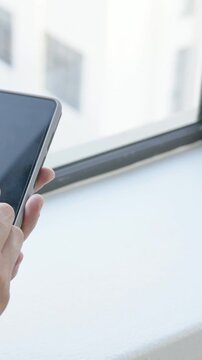 Vertical video: Sweatshirt hand tapping pen switching to thumb, swiping tablet by window