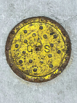 Yellow painted gas valve cover plate in the street pavement