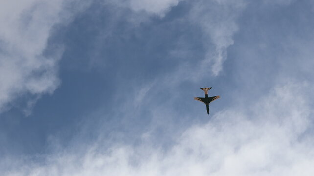 Single jet flying overhead through blue sky and wispy clouds
