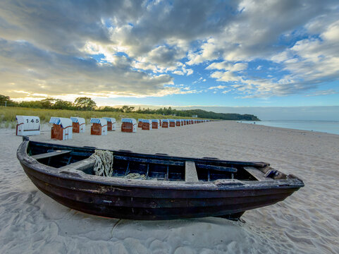 Altes Holzboot im Sand vor einer Reihe von Strandk&ouml;rben an einem Ostseestrand bei Sonnenuntergang, Baabe, R&uuml;gen, Deutschland