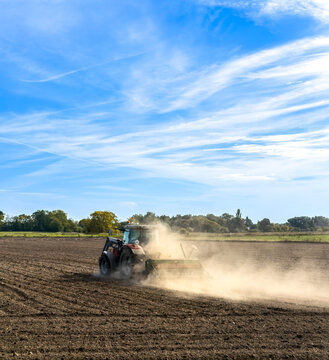 Roter Traktor bei der Aussaat auf einem staubigen Acker in weiter Landschaft unter bew&ouml;lktem Himmel, Berlin, Deutschland