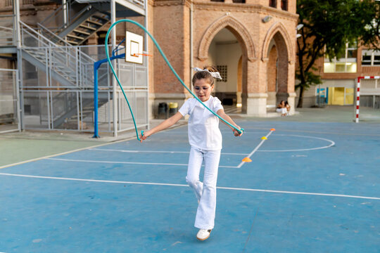 Young girl actively jumping rope on a blue school playground. Child having fun, exercising outdoors during playtime