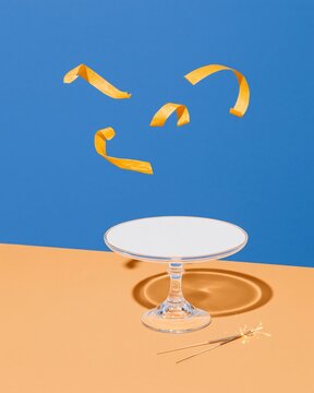 Empty clear glass cake stand with gold paper streamers swirling above, a crisp and minimal mockup for holiday party product displays