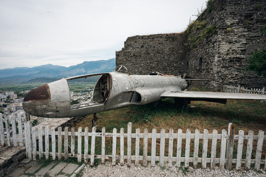 Old military airplane wreck displayed behind a wooden fence inside the stone walls of Gjirokaster Castle in Albania.