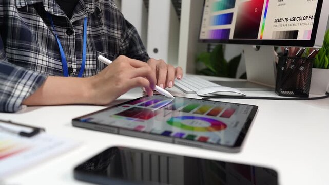 Interior designer selecting color palettes and reviewing home design concepts at a computer workstation, with a miniature house model and digital tablet on the desk.