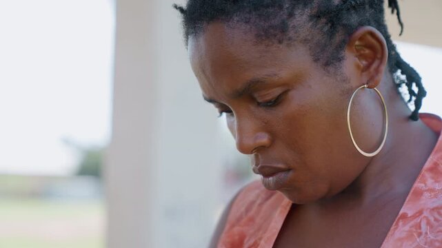 Close up portrait captures profile of lady wearing gold hoop earrings. Her hair features small dreadlocks and woman is dressed in orange patterned top. background remains softly blurred