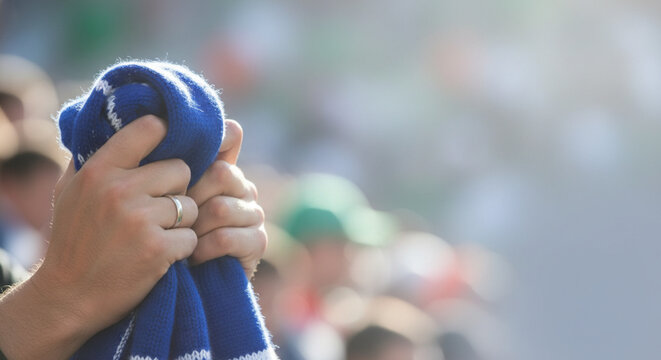 Close up of a person's hands holding a blue and white striped scarf at a sporting event with a blurred crowd in the background
