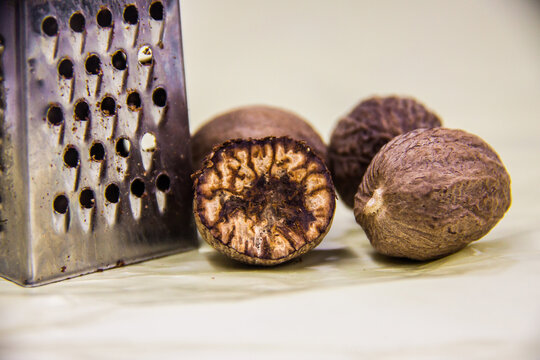 Macro food photo isolated on white background, sliced cut natural dry nutmeg, healthy vegetarian aromatic eatable spice, stainless steel grater, selective focus, shallow depth of field,  Cairo Egypt