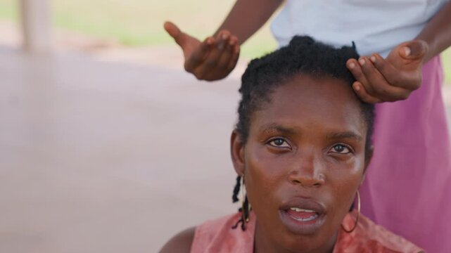 Close up shows stylist carefully working to style someone hair. scene focuses solely on hands and head with soft natural light and outdoor background visible through blur