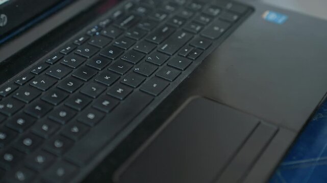 Close up of hands typing on black laptop with white lettering. Hands repeatedly press various key combinations while interacting with touchpad maintaining consistent focus on digital