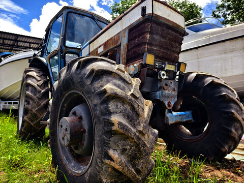 Weathered blue tractor parked beside farm buildings on grassy yard