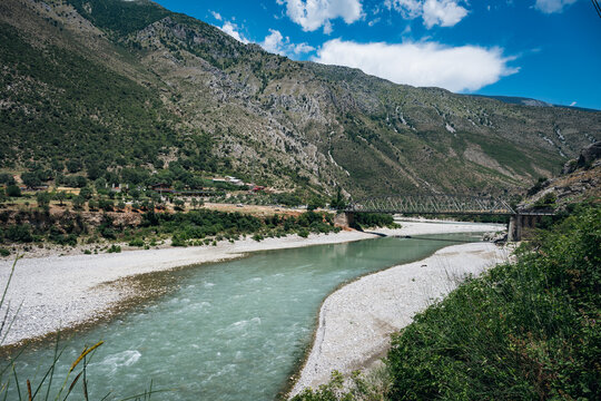Turquoise river flowing through a rocky valley surrounded by green mountains under a blue sky in Albania.